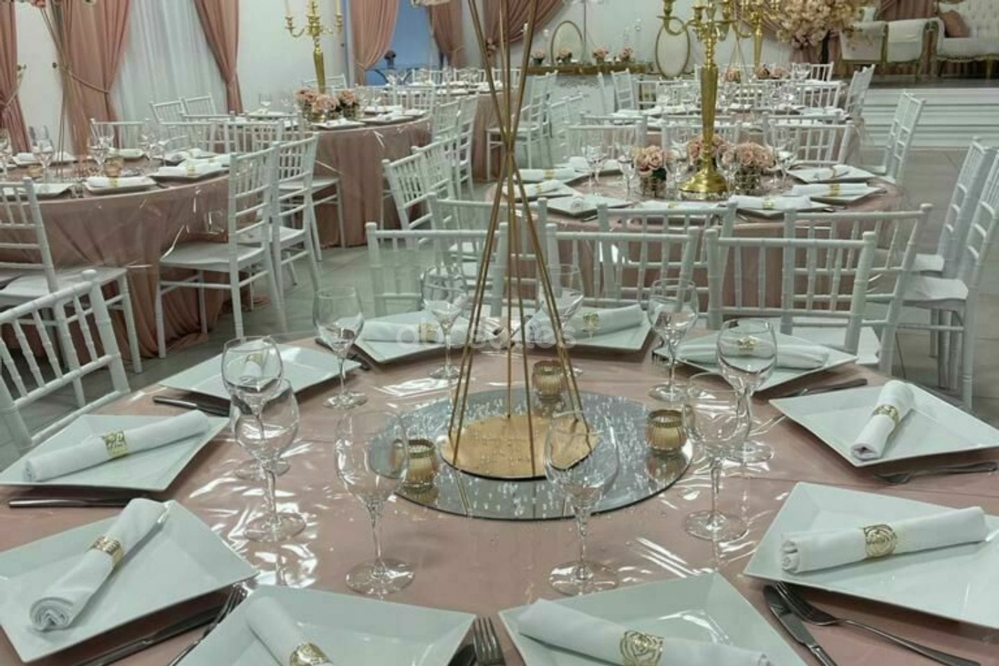 Table nappée de rose, assiettes carrées, serviettes blanches et chandelier doré.