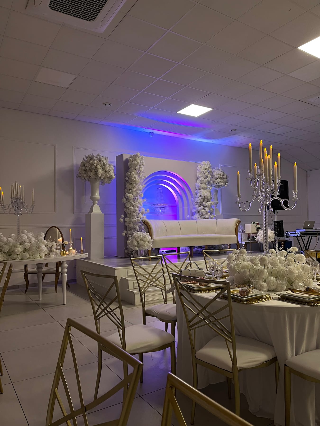 Salle de soirée éclairée en bleu et violet, tables dressées devant l'estrade.