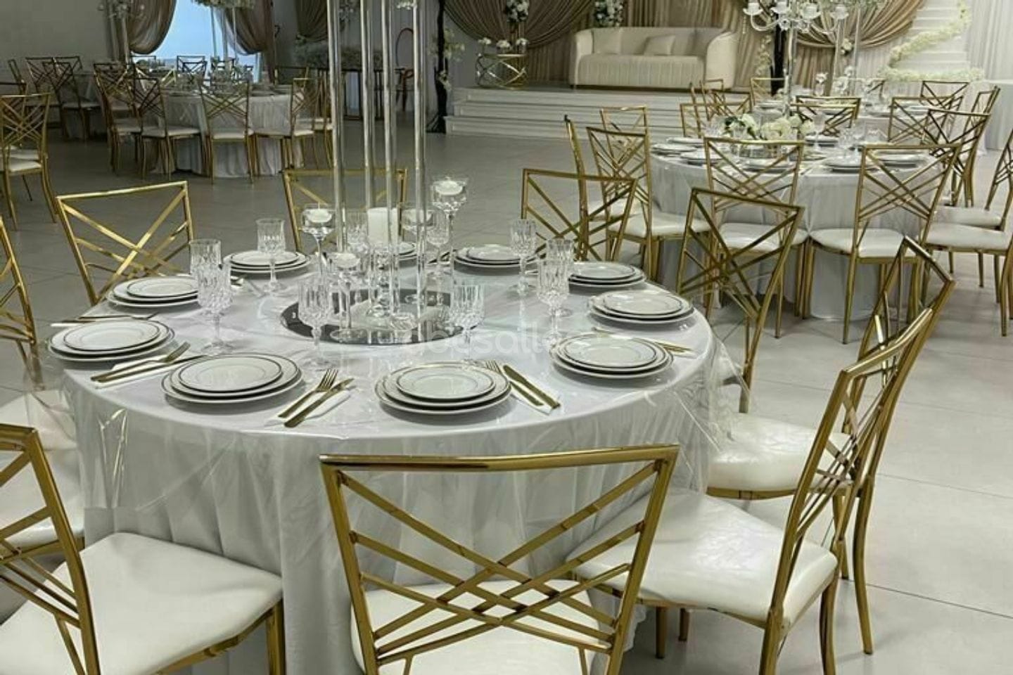 Tables nappées de blanc et chaises dorées à croisillons.
